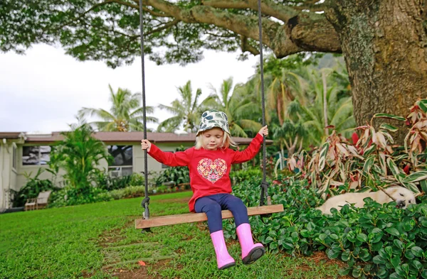 Cute little girl swinging on wooden swing outdoors — Stock Photo, Image