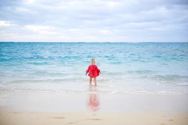 Little girl in red coat staying in the water on the beach — Stock Photo, Image