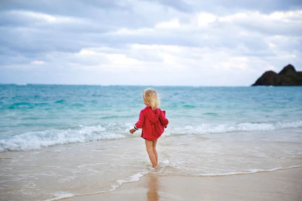 Little girl in red coat running into the water on the beach — Stock Photo, Image