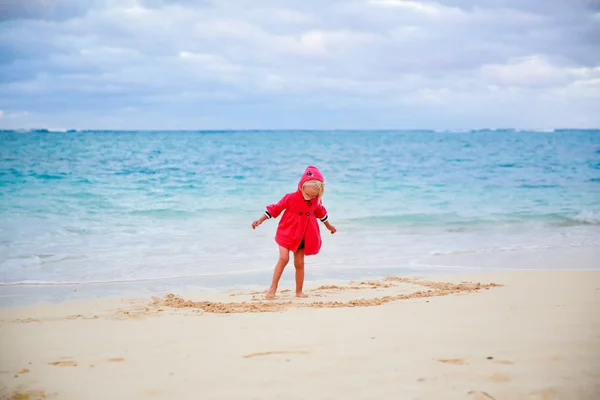 Little girl in red coat playing with sand on the beach — Stock Photo, Image