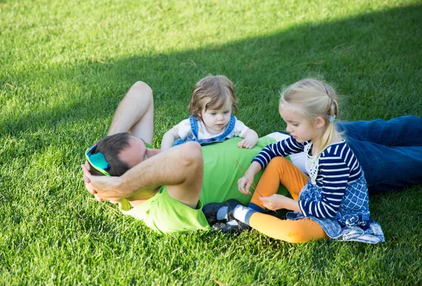 Joven padre con dos hijas tumbadas en la hierba en un parque — Foto de Stock