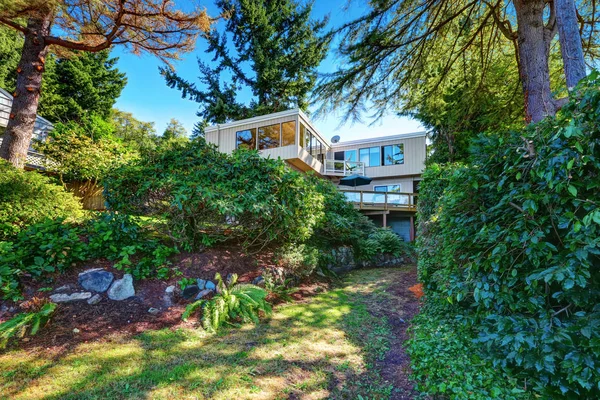 Beige house with large windows sinking in green bushes and trees. — Stock Photo, Image