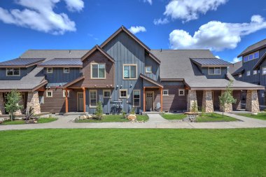 Doğal kahverengi ve gri renklerle, yürüyüş yolları, yeşil çimenler ve doğal taşlarla yeni inşa edilmiş modern ve kırsal bir ev. Mavi gökyüzü ve güneşli bir gün. Amerikan yeni mimarisi.