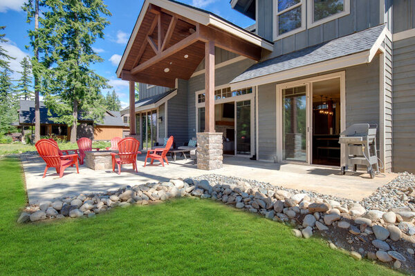 Huge open to nature Back yard with fire pit , amazing patio and red chairs near newly bild luxury real estate home with forest biew and green grass.