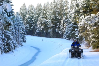 Man riding snowmobile or fourwheeler on the country side trail near water canal. clipart