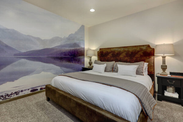 Calm evening cozy guest bedroom with large king size sued bed and purple mural. White linen and beige blanket.