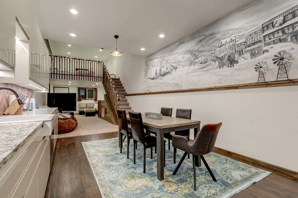 Dining room with rustic mural of old village and modern kitchen shiny beige cabinets, rustic brick backsplash.