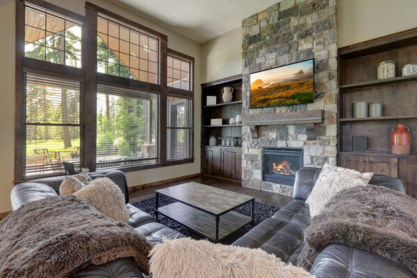 Luxury cozy living room interior with grey stone and rich wood with fuzzy blankets and large windows and TV.