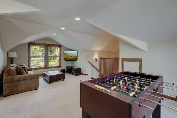 Hockey play table in upstairs family play room with vaulted ceiling with TV and sofa.