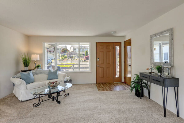 Older midcentury rambler interior with white ceiling and beige carpet, sofa, chairs and lake view.