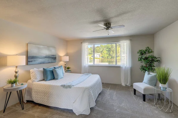 シンプルなベッドルームの新鮮なインテリア 白いベッド 青いアクセントと湖の景色大きな窓 — ストック写真