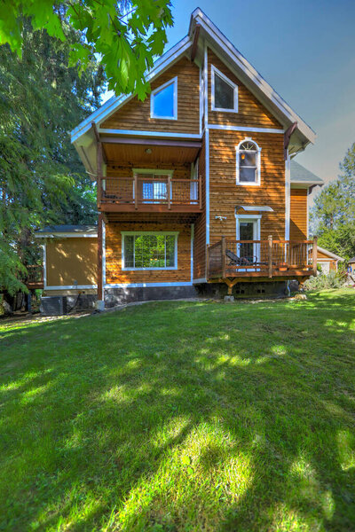 Wooden large American house with natural brown tone with white trim and green summer nature.