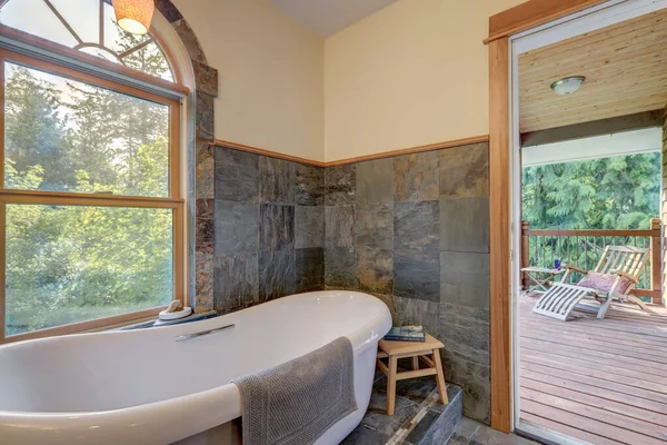 浴室内部有灰色瓷砖和自由站立的白色浴缸 阳台上有敞开的门 — 图库照片