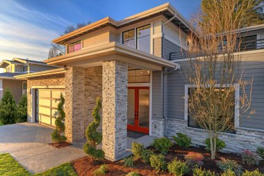 Lüks detayları olan modern çağdaş ev, peyzaj, taş, ahşap, cam, akşam ışıkları ve kırmızı ön kapısı olan büyük pencereler..