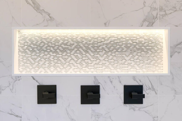 Details of the shower shelve with white marble and mosaic, light. Three handles, shower head in dark brass.