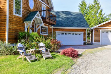 Beyaz süslemeli, doğal kahverengi tonu olan ahşap büyük Amerikan evi ve çift katlı garajlı yeşil yaz doğası..