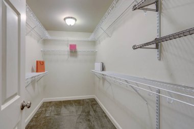 Basit metal rafları ve gri halısı olan büyük boş yatak odası dolabı..