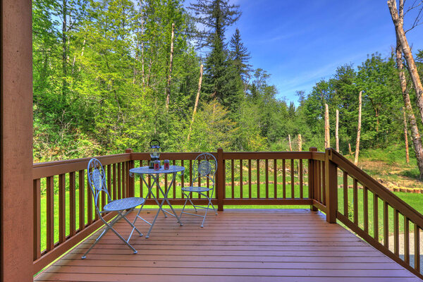 Simple wooden deck with metal chairs and table overlooking wild nature Northwest forest and swamp land.