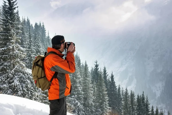 A man photographes of a winter, mountain landscape. Against the background of mountains and pines. Pictured from the back — Stock Photo, Image