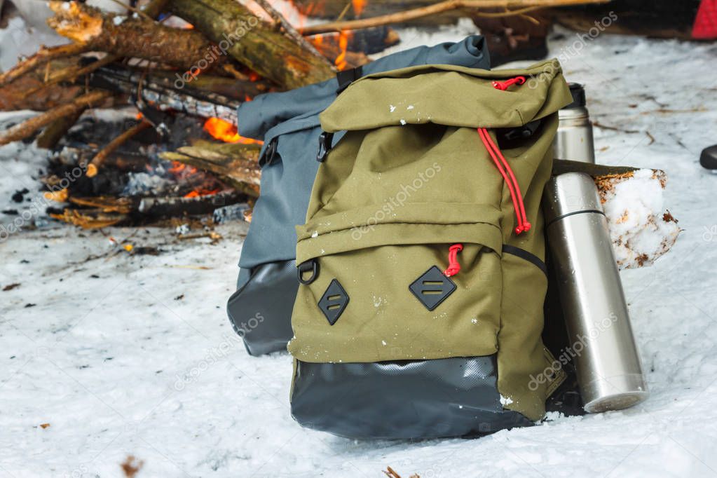 Backpacks in the background of a burning bonfire in the winter forest. Green backpack. Gray backpack.