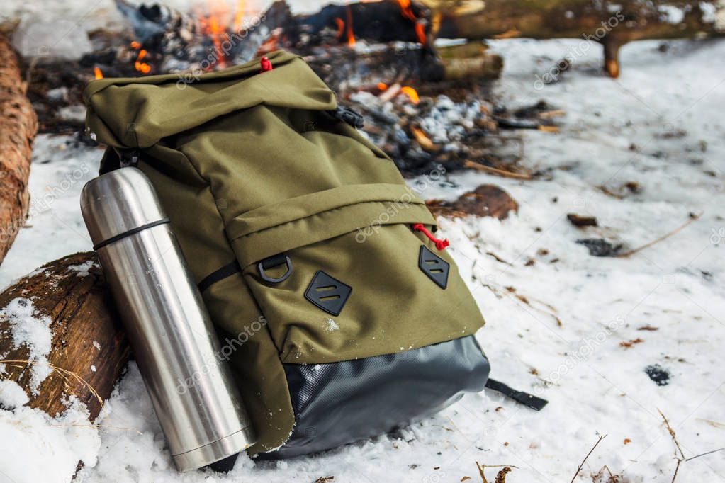 Backpack in the background of a burning bonfire in the winter forest. Green backpack.