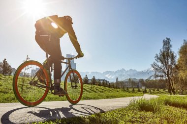Yeşil çim ve Dağları çerçevede bir şehirde bir yolda bir bisikletçi rides.