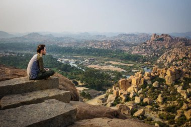 Bir tepenin kenarında oturan turist. Matanga tepesinden Hampi 'nin harabelerinin güzel manzarası. Karnataka, Hindistan