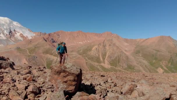 登山者爬上一块大石头 一个背着背包的旅行者站在山上的一块大石头上 四周是高山上有冰川的美丽景色 — 图库视频影像