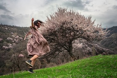 Kız, çiçek açan ağaçların arasında sevinçle dolanıyor. Bahar geldi.