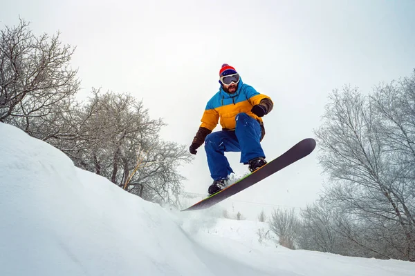 El tipo está haciendo snowboard. Salta de una colina nevada —  Fotos de Stock