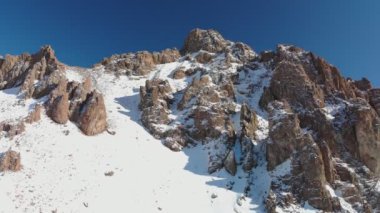 Tourists climb to the top of the mountain. Cliffs among the mountains in the snow. Amangeldy Peak a mountain peak in the small Almaty spur