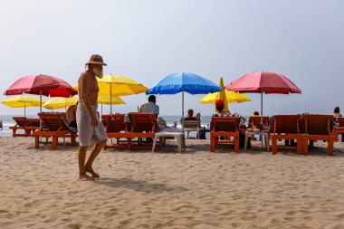 An elderly bearded man is walking along the beach. Carefree life in a tropical country.