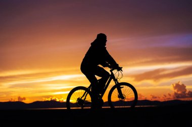 Güzel bir günbatımının arka planında yuvarlanan bir bisikletçinin silueti. Dağlarda muhteşem bir akşam