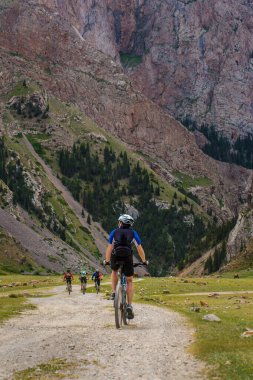 Bir grup turist dağlarda bisiklet sürüyor. Arkadan manzara. Kırgızistan
