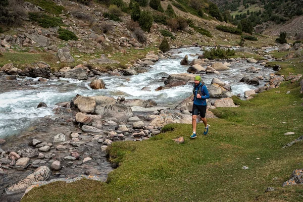 Athlete runs near a mountain river. Runner guy is jogging in the highlands. Man is training outdoors. Trail running