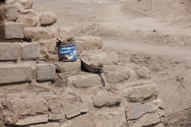 PACHACAMAC, LIMA / PERU - May 10 2016:  A bucket of mud with a paint brush and a metal scoop resting on a mud brick wall that is being repaired at Pachacamac archeological site.