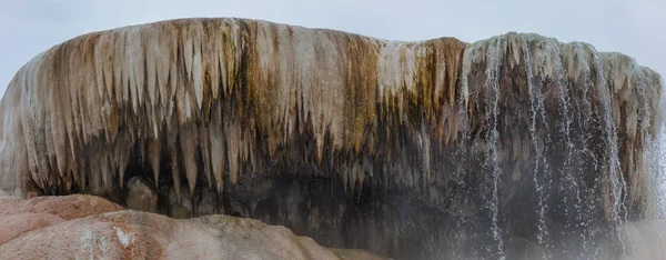 Hot water cascades off of a travertine feature with stalactites hanging down and hot steam floating up at Mammoth Hot Springs, Wyoming.