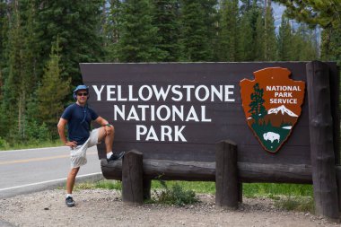 Yellowstone Ulusal Parkı, Montana, ABD - 13 Temmuz 2014: Genç bir turist 13 Temmuz 2014 tarihinde Montana 'da 212. Otoyol' un kuzeydoğu girişinde Yellowstone Ulusal Parkı için ahşap bir tabelanın yanında duruyor..