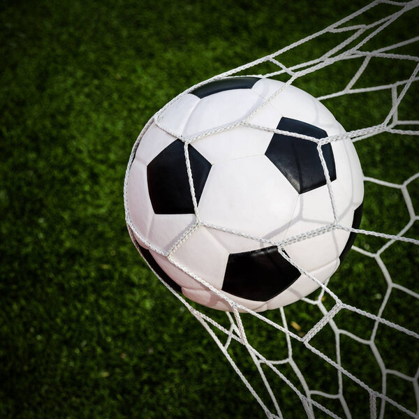 Soccer football in Goal net with green grass field.