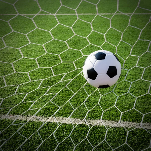 Soccer football in Goal net with green grass field. Stock Image