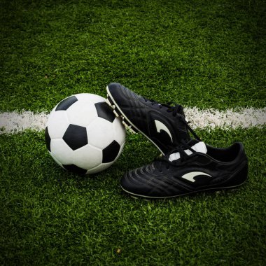 Futbol topu ve yeşil çim sahası üzerinde ayakkabı.