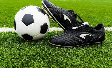 Futbol topu ve yeşil çim sahası üzerinde ayakkabı.