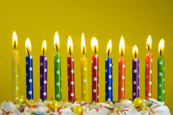 Bougies multicolores brûlent sur un gâteau d'anniversaire sur un fond jaune — Photo