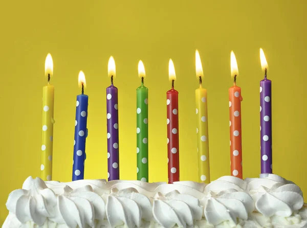 Різнокольорові свічки горять на день народження торт на жовтому фоні — стокове фото