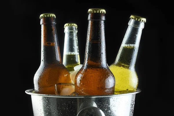 Botellas de cerveza en un cubo con hielo sobre un fondo negro — Foto de Stock