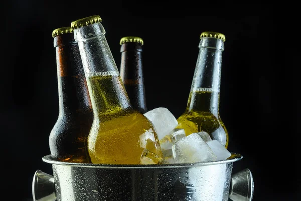 Bierflessen in een emmer met ijs op een zwarte achtergrond — Stockfoto