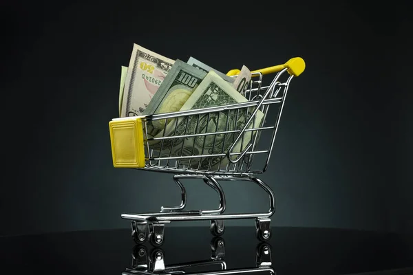 Close up of american dollar banknotes on shopping cart over dark background — Stock Photo, Image