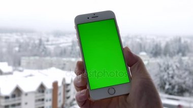 Adam kendi özel içerik ve kar doğa arka plan için yeşil bir ekran ile boş bir akıllı telefon tutar.