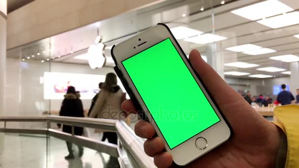 Mujer sostiene un dispositivo inteligente en blanco con una pantalla verde para su propio contenido personalizado en frente de la tienda de Apple — Vídeo de stock