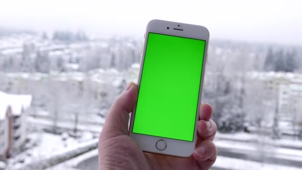 Pan tiro do homem detém um telefone inteligente em branco com uma tela verde para o seu próprio conteúdo personalizado e neve natureza fundo . — Vídeo de Stock